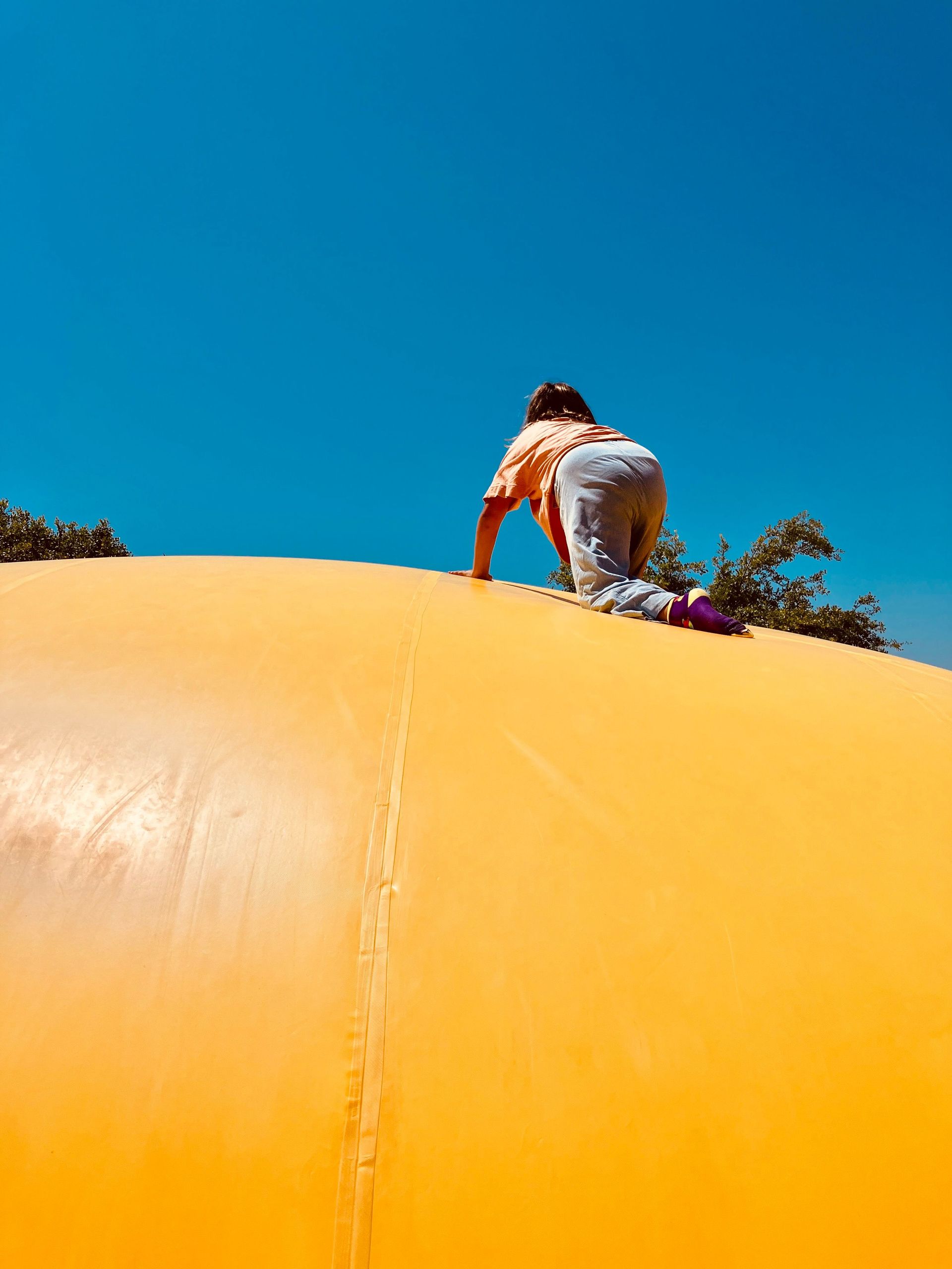 Child climbing a large yellow inflatable dome outdoors on a sunny day.