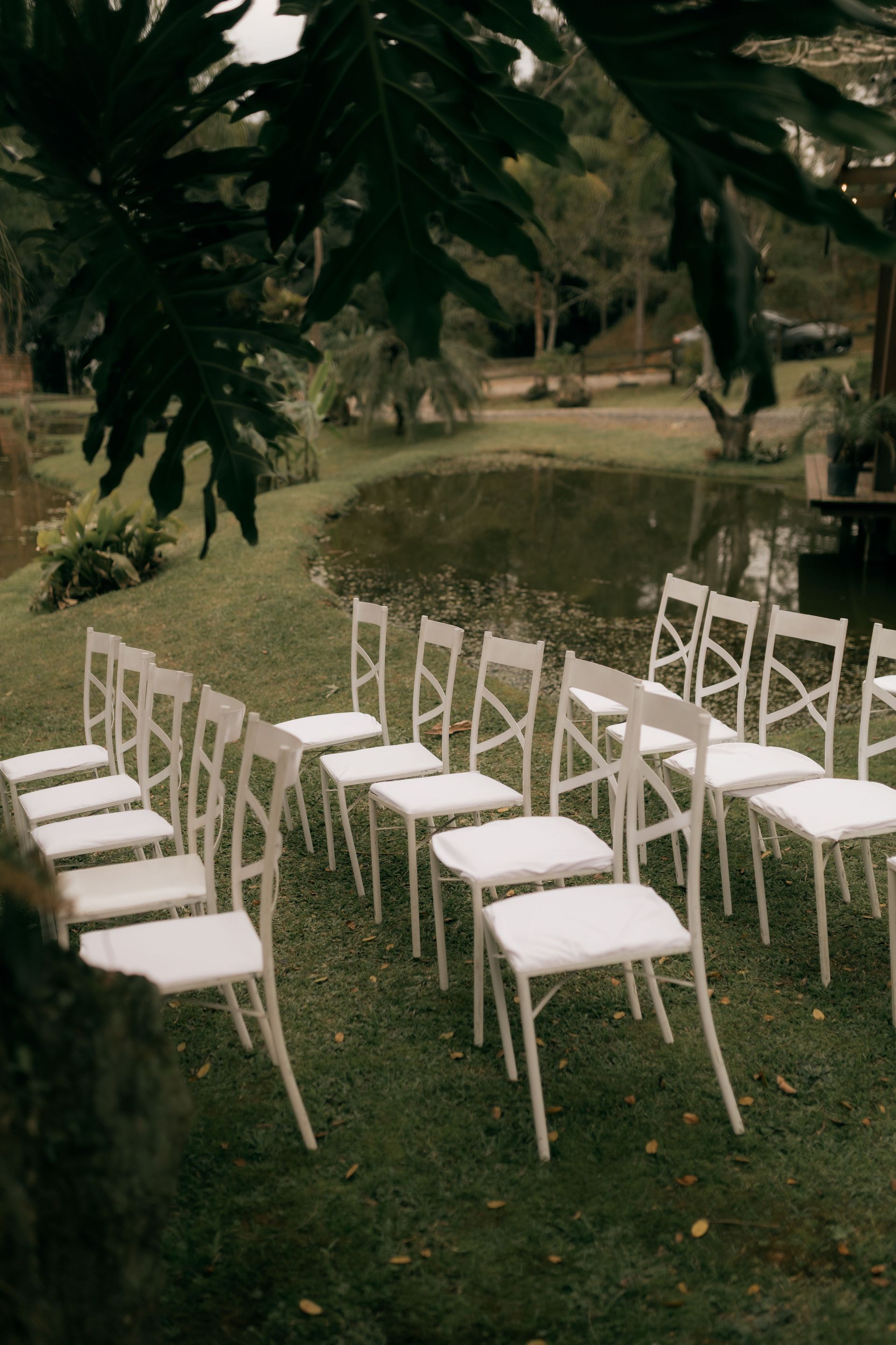 Elegant outdoor setup with white chairs arranged by a serene pond, ideal for weddings.