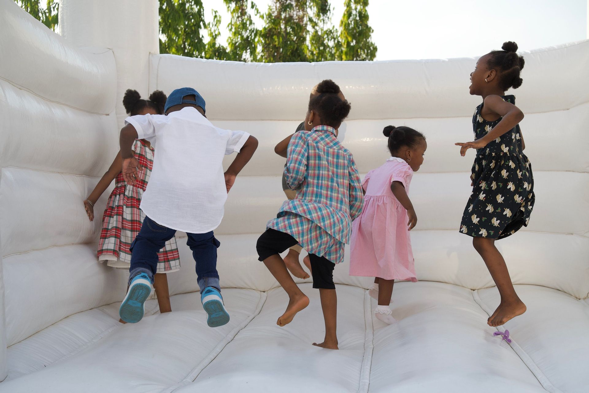Happy kids jumping on a white bouncy castle, enjoying a sunny day outdoors.